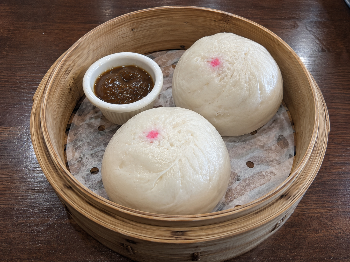 Steamed asado siopao buns with sweet sauce in a bamboo steamer