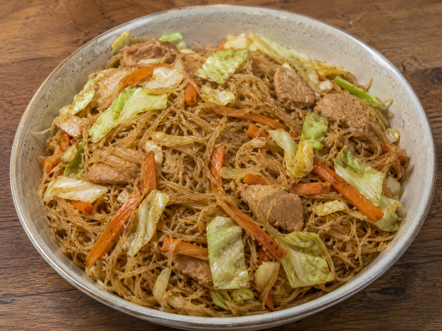 Bowl of Pancit Bihon — thin rice noodles with chicken, cabbage, and carrots